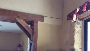 Quarto com televisão em suporte, estrutura de vigas de madeira e parede de pedra.