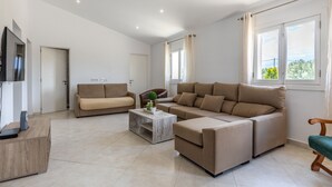 Un vaste espace de vie comprenant un grand canapé beige, un canapé plus petit, une table basse et un téléviseur posé sur un meuble en bois.