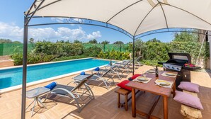 Un espace aménagé au bord de la piscine, avec des chaises longues, un barbecue et une table dressée pour les repas.