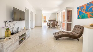 Un vaste espace de vie doté d’un téléviseur à écran plat fixé au mur, d’un canapé confortable et d’un coin repas situé à l’arrière-plan.