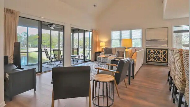 Ein geräumiger Wohnbereich mit großem Fenster, Deckenventilator und einer Sitzecke mit Sofa und Sesseln.