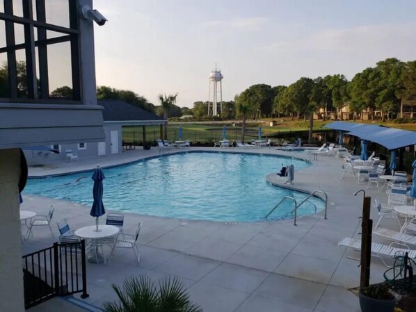 Una piscina con sillas de descanso y sombrillas, una torre de agua al fondo y vistas a un campo de golf.