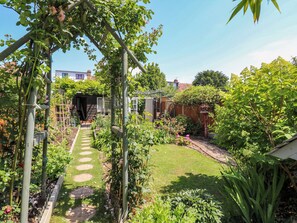 Un jardin avec un sentier, une clôture en bois et différentes plantes.