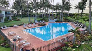 Une piscine dotée de chaises longues et entourée d’une clôture, le tout bordé de palmiers et adossé à un bâtiment.