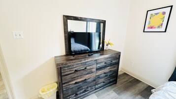 A bedroom with a wooden dresser, a mirror, a bed, and a small trash bin.