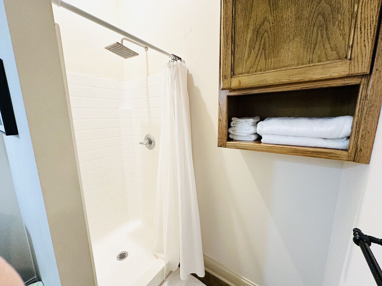 A bathroom with a shower, a white towel rack, and a wooden cabinet.