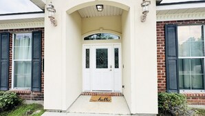 Une maison avec une porte d’entrée blanche, un petit porche et un paillasson sur lequel est écrit « Bonjour ».