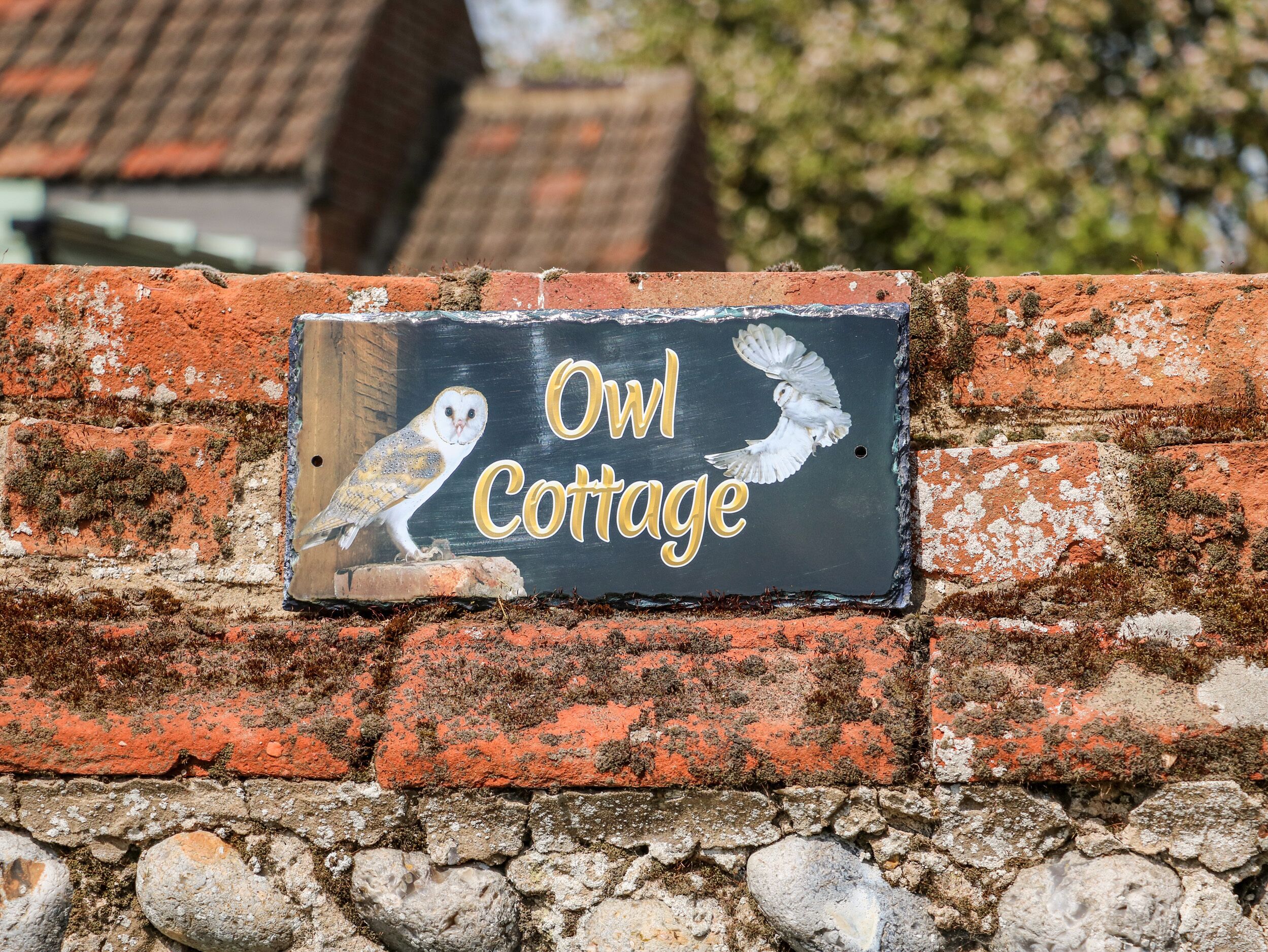 Un mur de briques sur lequel est affiché un panneau indiquant « Owl Cottage ».