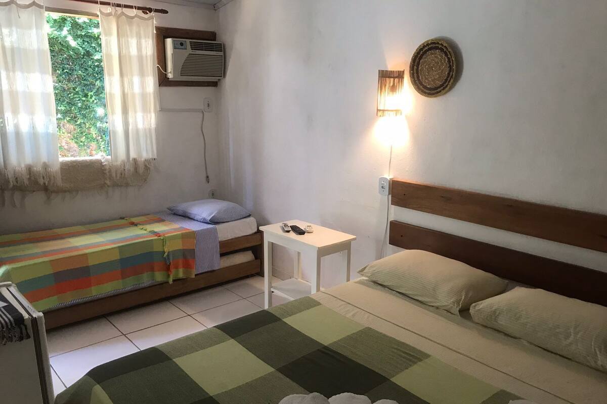Una habitación con dos camas, una mesita, un aire acondicionado y una lámpara fijada a la pared.