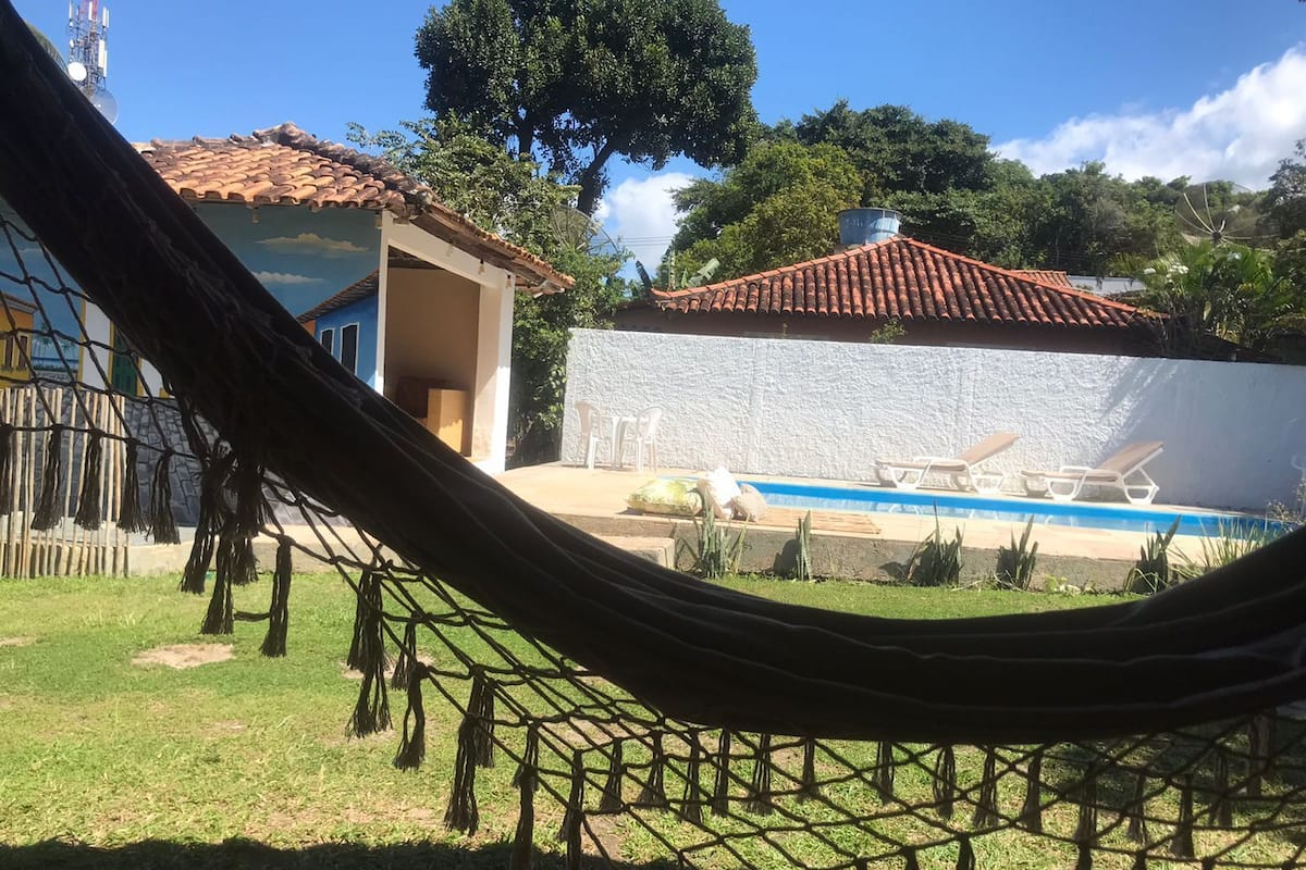 Una hamaca en un patio trasero con una piscina, una pared blanca y un edificio con techo de tejas rojas.