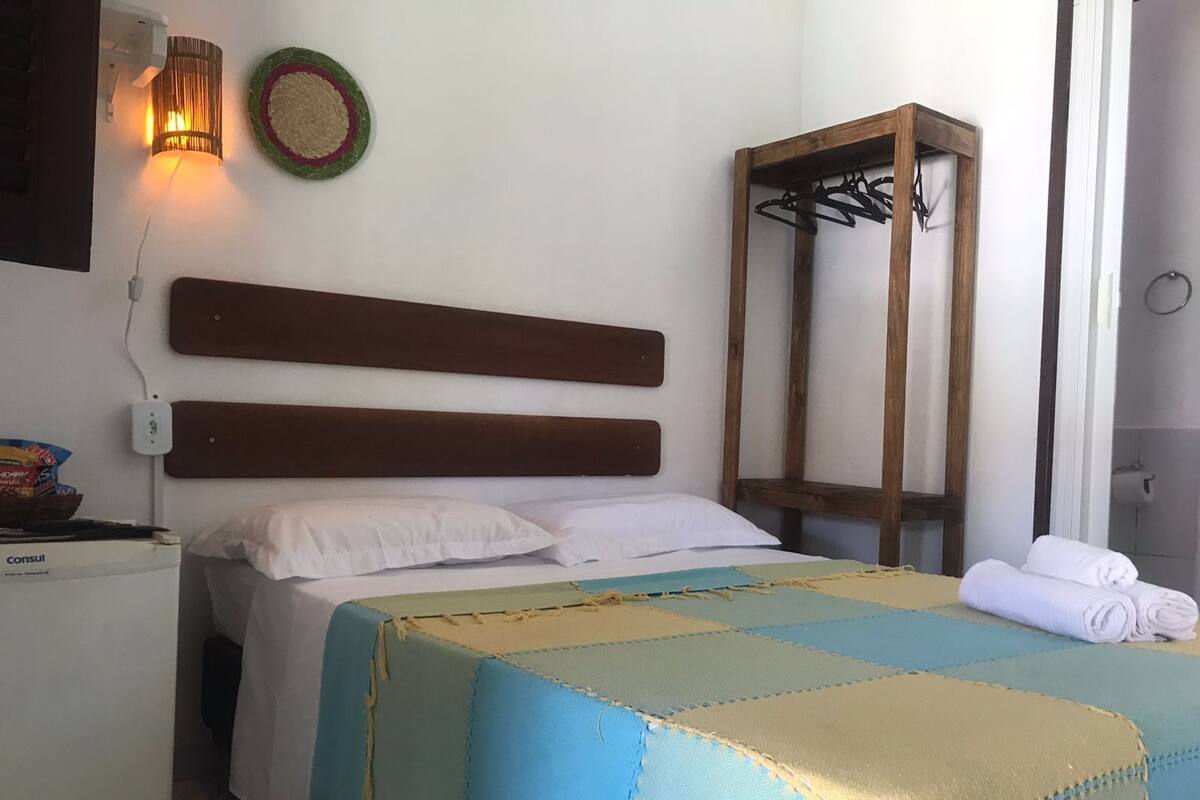 Habitación de hotel ordenada con cama, mesita de noche, lámpara y toallero en la pared.