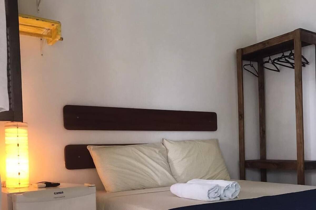 Una habitación de hotel con cama, mesita de noche, lámpara y armario.