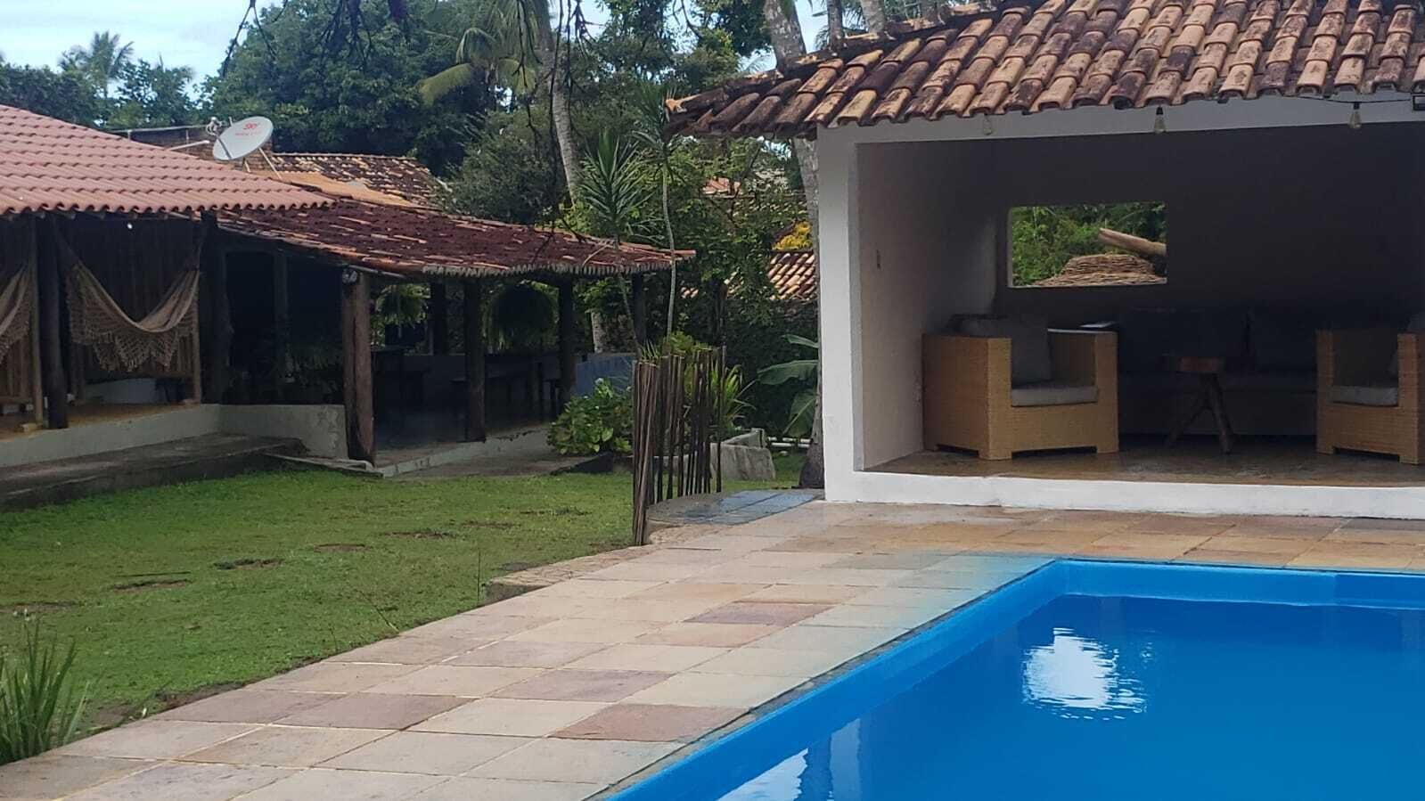 Una piscina con solárium de baldosas, un espacio de estar al aire libre cubierto y una antena parabólica en un edificio.