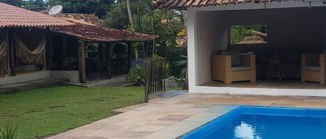 Una piscina con solárium de baldosas, un espacio de estar al aire libre cubierto y una antena parabólica en un edificio.
