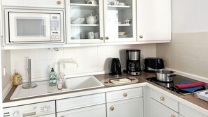 A modern kitchen with white cabinets, a built-in microwave, a coffee maker, a toaster, and a sink. - North Sea Residence App 23 Westerland (Westerland)