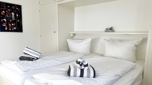 A double bed with white bedding, a striped towel, and a small decorative item on the headboard. - North Sea Residence App 23 Westerland (Westerland)