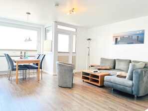 Een moderne woonkamer met een grijze bank, een houten salontafel en een eethoek met een tafel en stoelen.