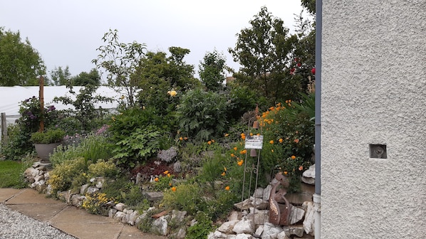 A garden with various plants and flowers, a stone wall, and a metal sculpture. - 22 m² studio for 2–3 people + on-site parking, 5 km from Chambéry, 10 km from Aix-les-Bains (SONNAZ)