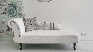 A white leather sofa with decorative pillows, a wall with floral artwork, and a modern wall clock. - Naturist Village - Le Diamond X Héliopolis Luxe, Naturist Village (Agde)