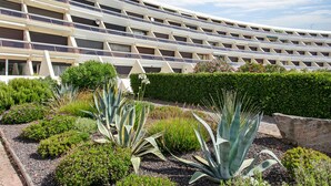A modern building with a curved facade, multiple balconies, and a landscaped garden with various plants. - Naturist Village - Le Diamond X Héliopolis Luxe, Naturist Village (Agde)