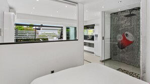 Une chambre d’hôtel moderne dotée d’un grand lit, d’une cloison en verre, d’un coin cuisine et d’un mur au motif de briques.
