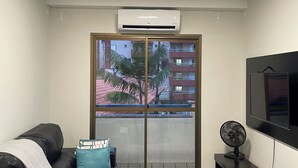 Una sala de estar con sofá, televisor y balcón con vista a edificios.