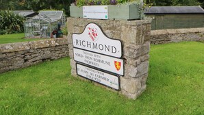 Un cartel con 'Richmond' y nombres de ciudades gemelas, una cama de flores y un invernadero.