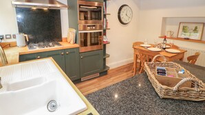 Una cocina con estufa, horno y lavamanos, un comedor con mesa y sillas, y un reloj en la pared.
