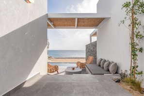 Relax in comfort with wicker furniture and a cushioned bench, surrounded by a shaded area with a serene beach view.