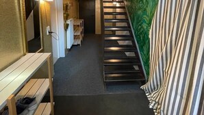 Un intérieur moderne avec un escalier, un mur miroir et un banc où sont posées des chaussures.