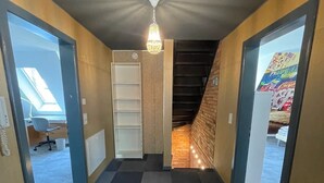 Un couloir doté d’un sol à carreaux, d’un lustre, d’un escalier et d’une porte donnant sur une pièce avec vue.