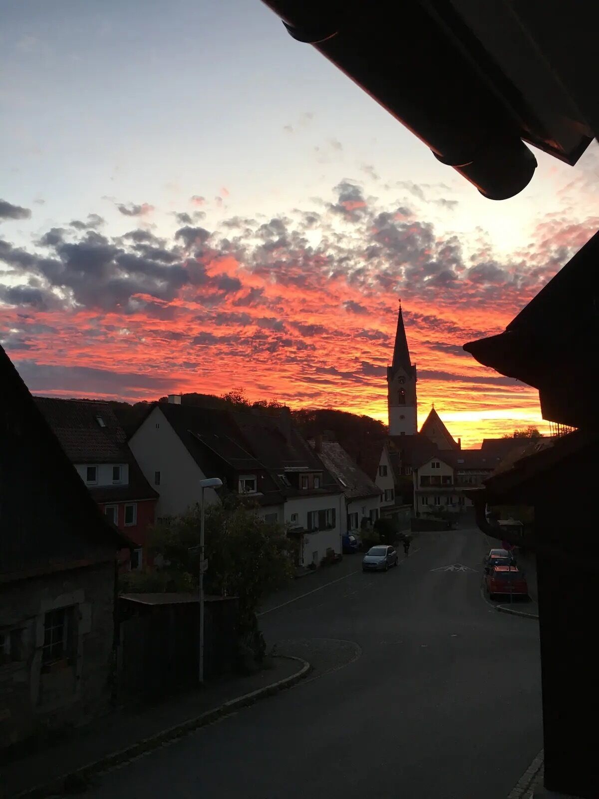 Vista da rua ao pôr do sol, com uma torre de igreja imponente ao fundo.