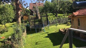 Un jardin avec un trampoline, une cabane en bois et une zone délimitée par une clôture.