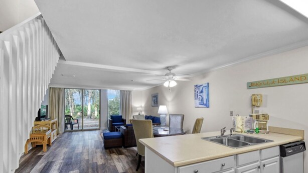 A modern kitchen with a central island, a dining area with blue chairs, and a large sliding glass door leading to a patio. - Villa 452 - lovely condo just steps away from pool and beaches (Jekyll Island)
