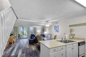 A modern kitchen with a central island, a dining area with blue chairs, and a large sliding glass door leading to a patio.