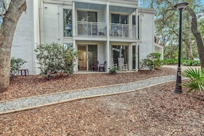 A two-story building with a balcony, a covered porch, and a gravel pathway leading to the entrance.