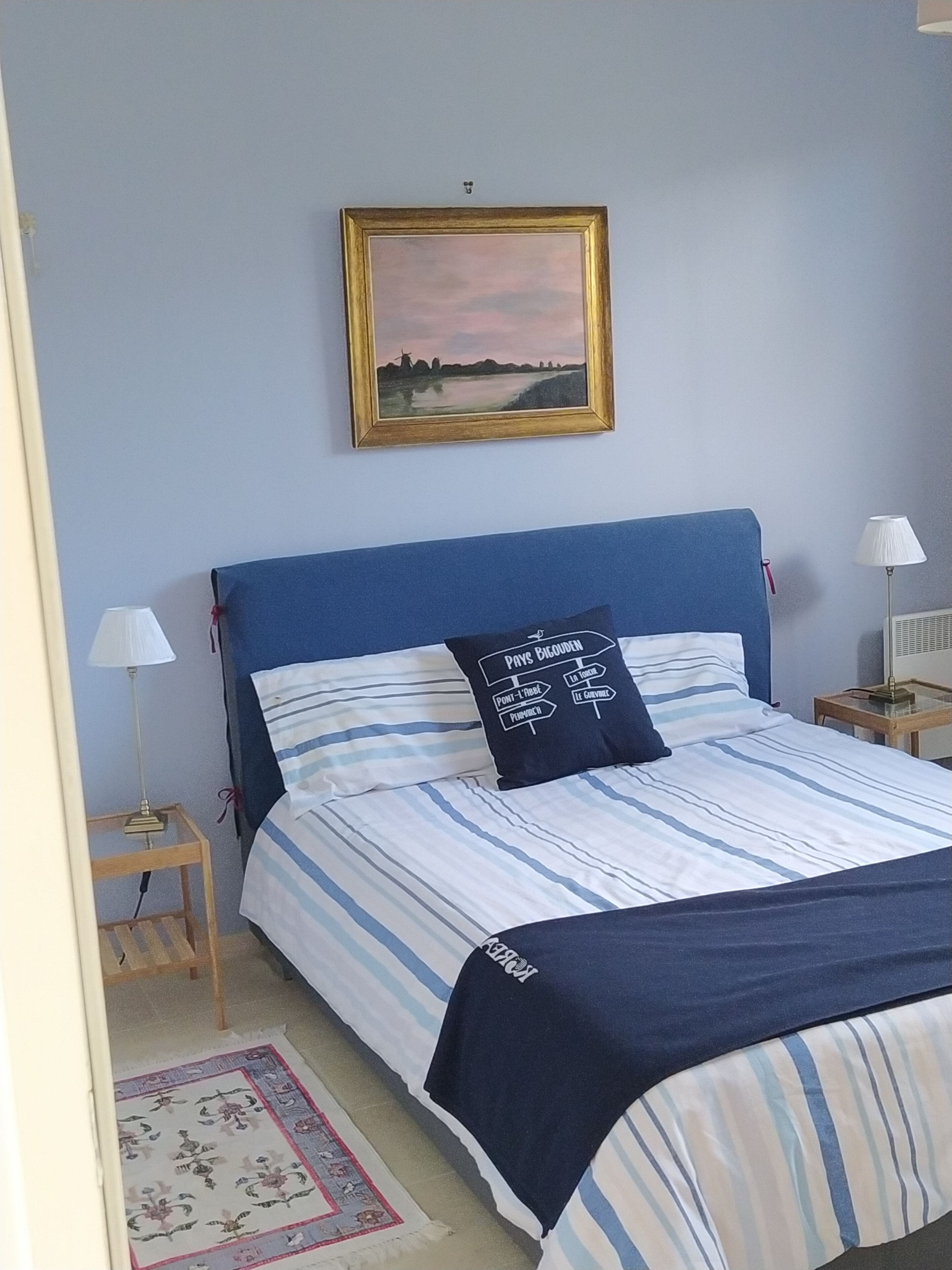 A bedroom with a bed, a nightstand, a lamp, a framed picture on the wall, and a rug.