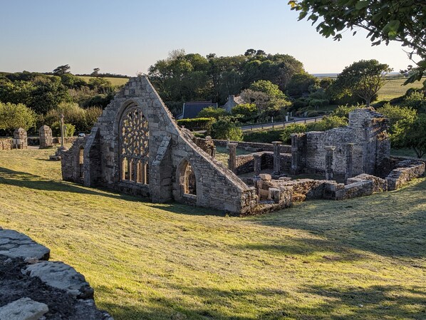 An ancient stone structure with arched windows and a central tower, surrounded by grassy fields and trees.