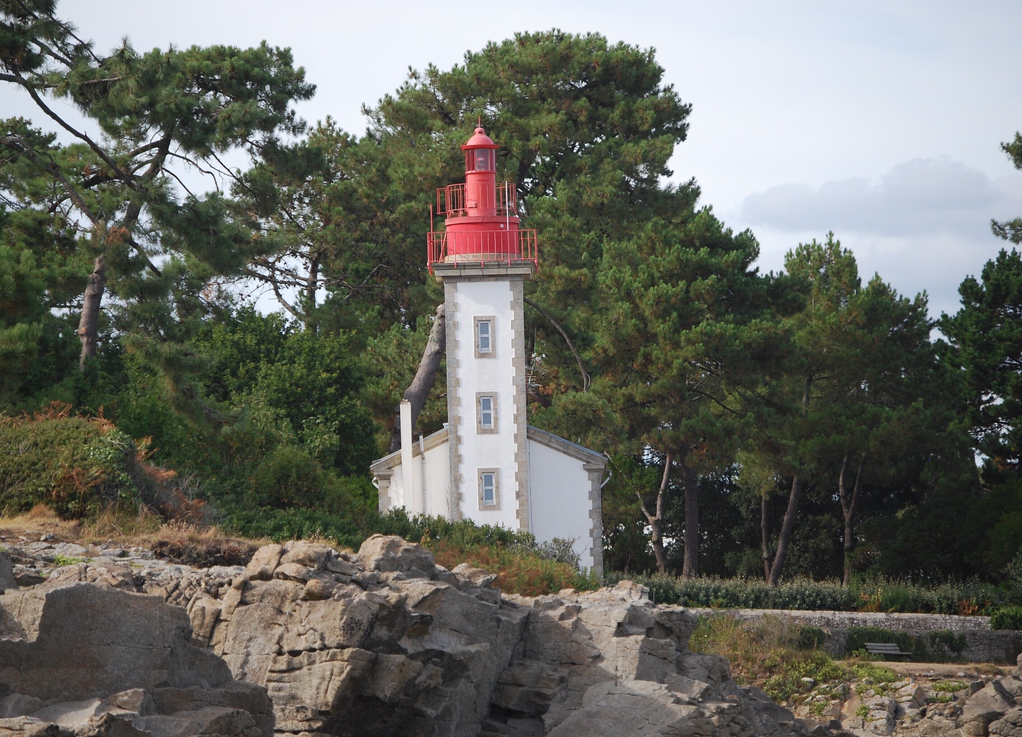 A lighthouse with a red top, surrounded by trees and rocky terrain.