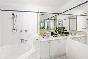 A modern bathroom with a bathtub, two sinks, a large mirror, and a shower. - Charming Seaside Apartment with Balcony & Pool, Steps from Trinity Beach (Trinity Beach)