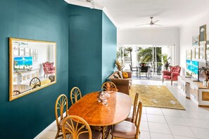 A dining area with a round table, chairs, and a large mirror on the wall. - Charming Seaside Apartment with Balcony & Pool, Steps from Trinity Beach (Trinity Beach)