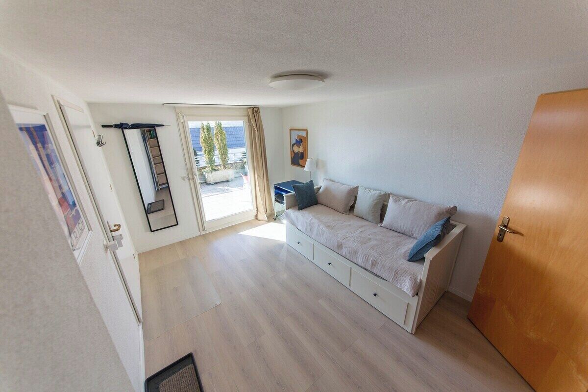 A room with a sofa, a door, a window, and a view of the outside.