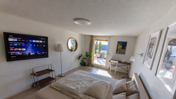 Une chambre d’hôtel moderne équipée d’un grand lit, d’un bureau et d’un téléviseur à écran plat diffusant diverses chaînes.