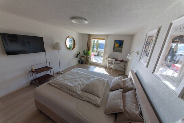 A bedroom with a bed, a desk, a TV, and a window.