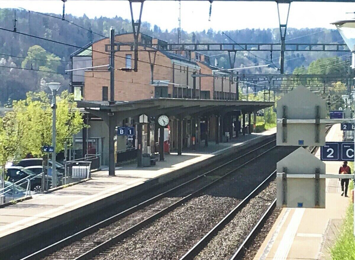 A train station platform with a clock, a shelter, and a building in the background.