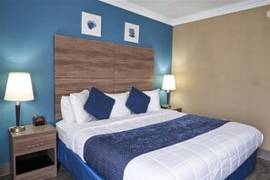 A hotel room with a large bed, two bedside lamps, a wooden headboard, and two wall-mounted artwork pieces. - King Bed Standard View (Fairhaven)