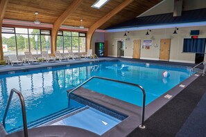 Una piscina interior con agua cristalina, un trampolín y sillas de descanso.