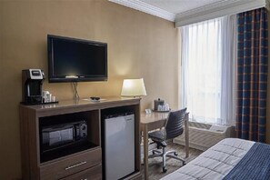 Une chambre d’hôtel équipée d’un lit, d’un bureau avec un ordinateur, d’une télévision, d’un mini-réfrigérateur, d’un four à micro-ondes, d’une machine à café et d’une lampe.