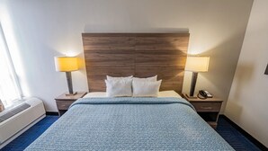 A hotel room with a large bed, two bedside tables, a wooden headboard, and a window with curtains.