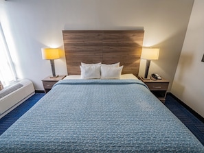 Una habitación de hotel con una cama grande, dos mesitas de noche, un cabecero de madera y una ventana con cortinas.